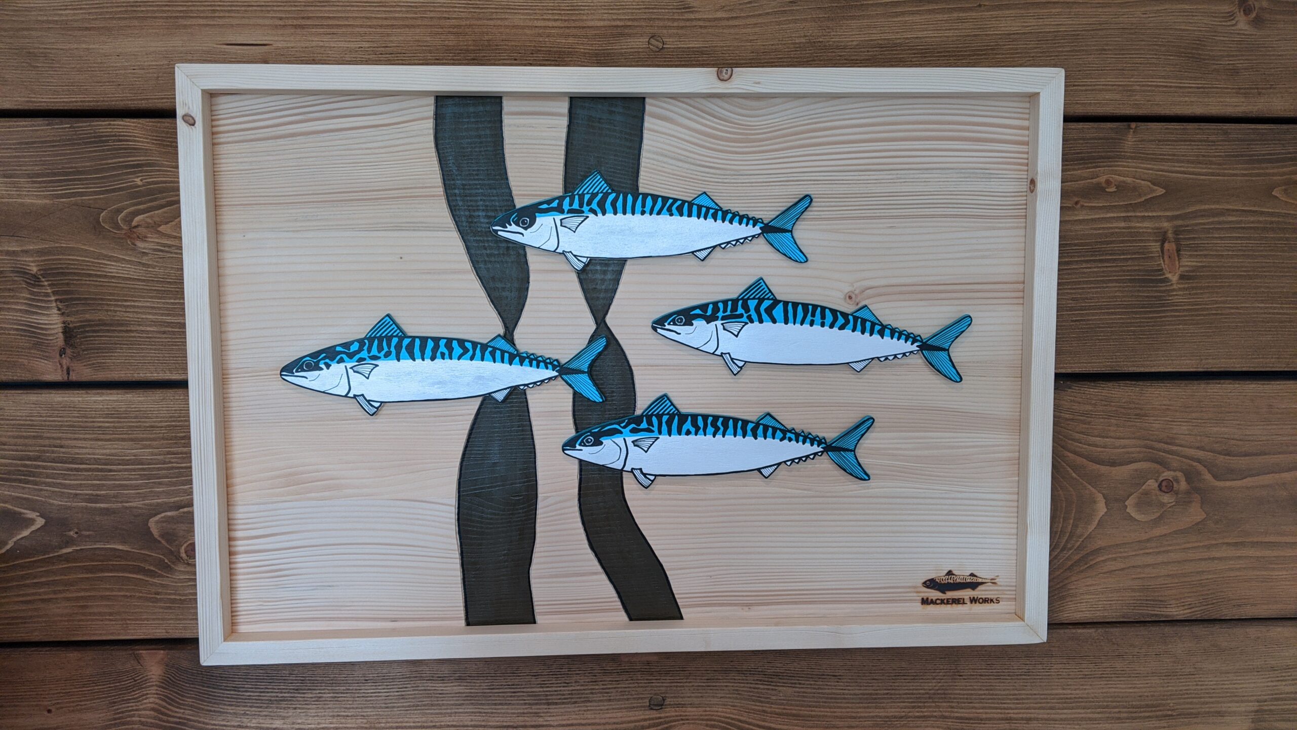 Four hand painted mackerel cutouts arranged as a shoal on a wooden background in a wooden frame